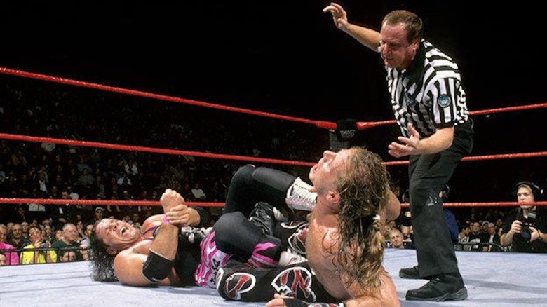 Bret Hart applies the figure four leglock to Shawn Michaels as Earl Hebner looks on