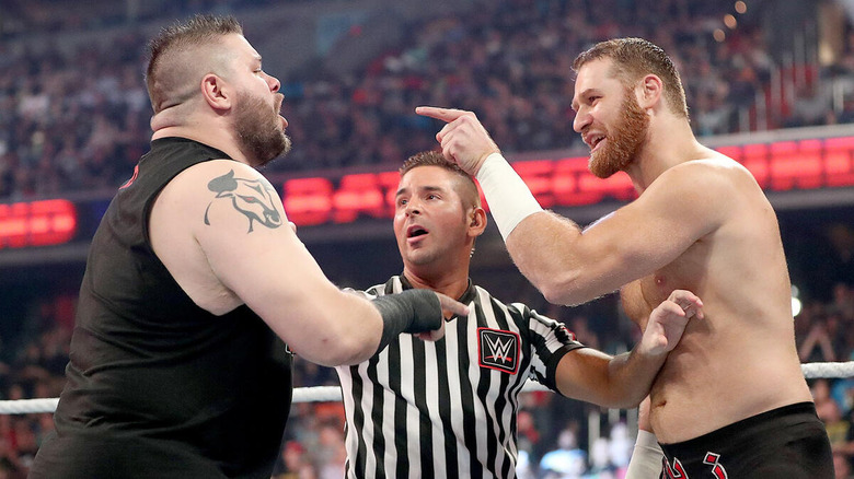 Kevin Owens and Sami Zayn point and yell at each other with a referee between them