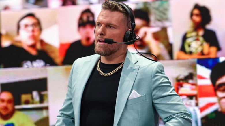 Pat McAfee stands behind the WWE commentary desk, wearing a headset, on an episode of WWE TV.