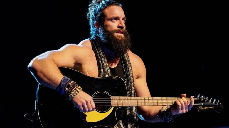 Former WWE star Elias sits in the middle of the ring, strumming on his guitar, during a performance on WWE television.