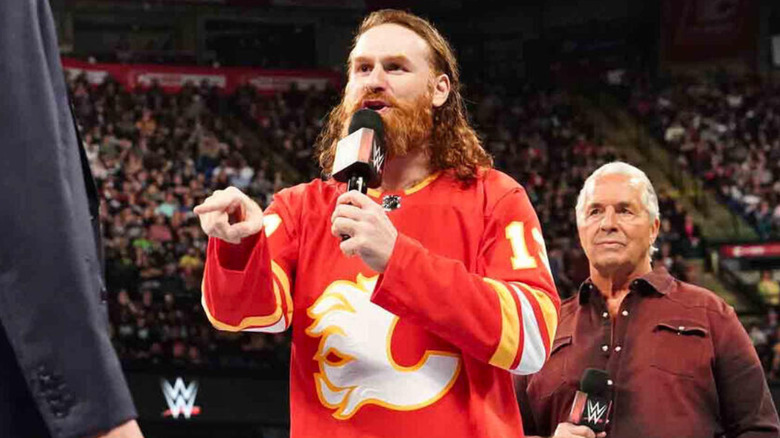 Sami Zayn holding a microphone while Bret Hart stands in the background