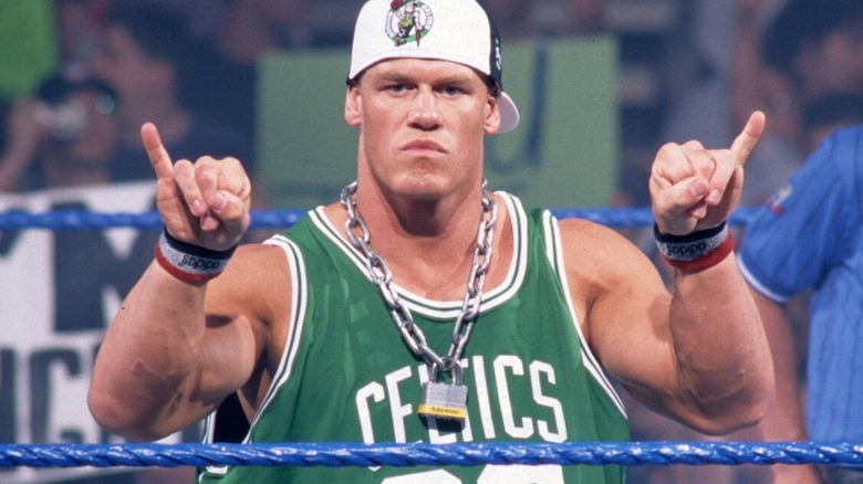 John Cena poses in the ring, wearing a ballcap and Boston Celtics jersey, before a match on WWE programming.