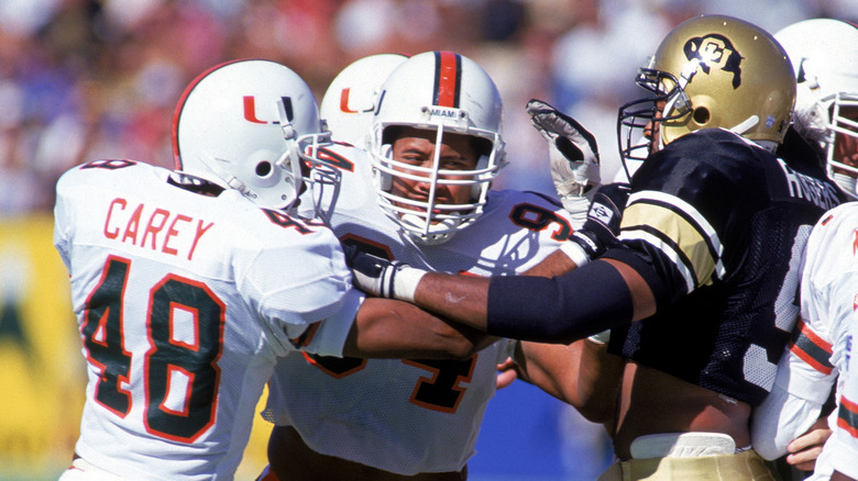 Defensive end Dwayne Johnson #94 of the University of Miami Hurricanes helps a teammate with a block during the NCAA game against University of Colorado Buffaloes on September 25, 1994. Dwayne Johnson is also known as "The Rock" of World Wrestling Federation.