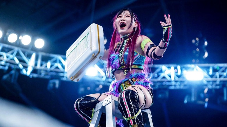 IYO SKY sits atop a ladder, holding the Money in the Bank briefcase after winning the match.