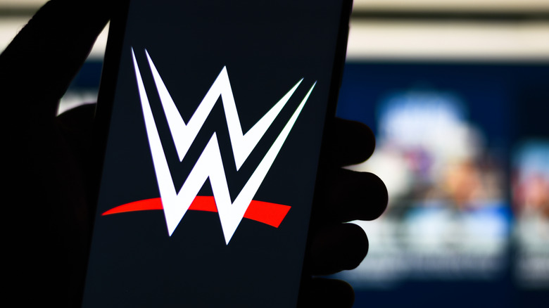 A WWE logo in scene on a phone someone is holding in front of a television screen, in a stock image.