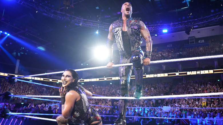 Damian Priest and Rhea Ripley pose on the ring ropes before a mixed tag team match at a WWE event.