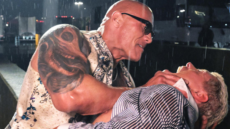 Dwayne "The Rock" Johnson holds Cody Rhodes' chin in a vice grip as rain falls around them.