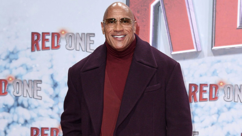 Dwayne "The Rock" Johnson poses in a maroon coat, a red turtleneck, and tinted shades for the premiere of "Red One."