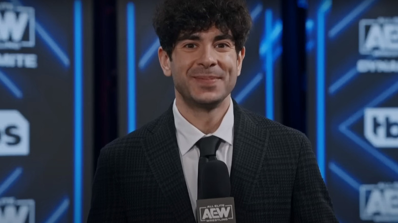 Tony Khan smiling while holding a microphone