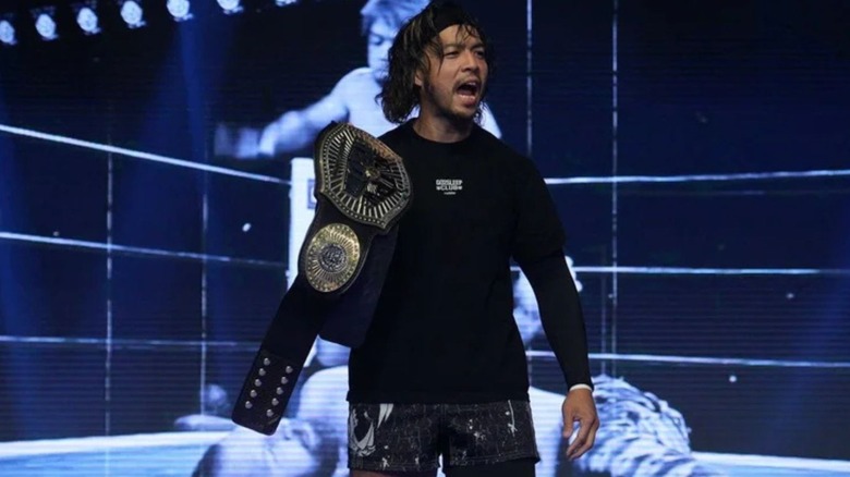 KENTA holds up a championship belt while speaking to an audience in a photo posted by Impact Wrestling.