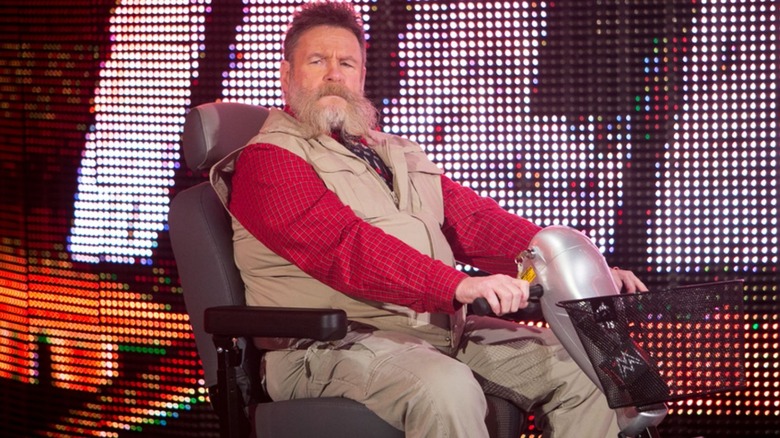 Dutch Mantell, known as Zeb Coulter in WWE, sits on stage in a motorized wheelchair during a segment on WWE TV.