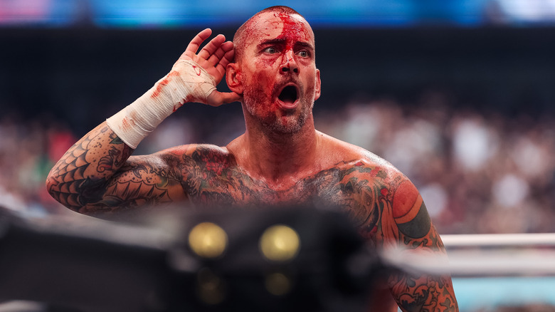 A bloody CM Punk holds a hand to his ear