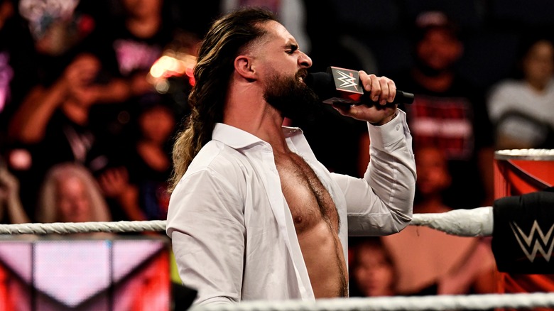 Seth Rollins wearing white dress shirt holding microphone up to his face