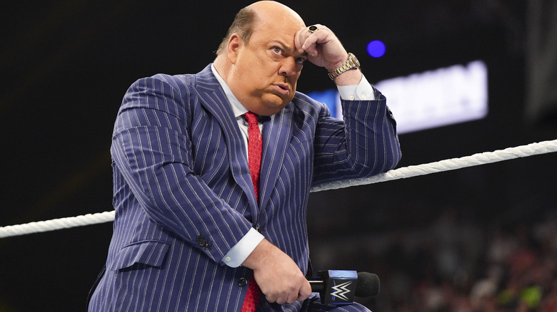 Paul Heyman with a microphone in one hand and his other hand on his forehead