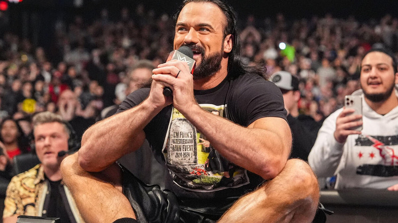 Drew McIntyre speaking into the microphone while sitting cross-legged on the announce table on "WWE Raw."