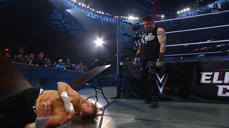 Owens standing over Zayn after crashing through the two tables