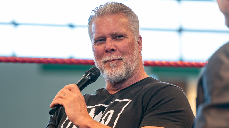 Kevin Nash speaks into microphone in wrestling ring while wearing NWO shirt