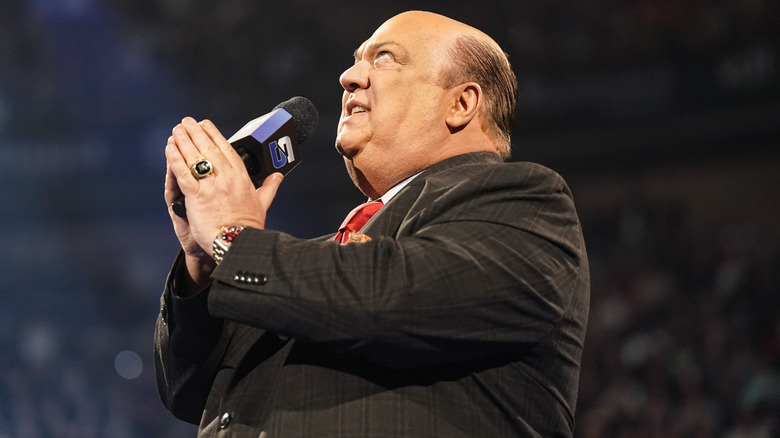 Paul Heyman holding a WWE SmackDown microphone and looking up