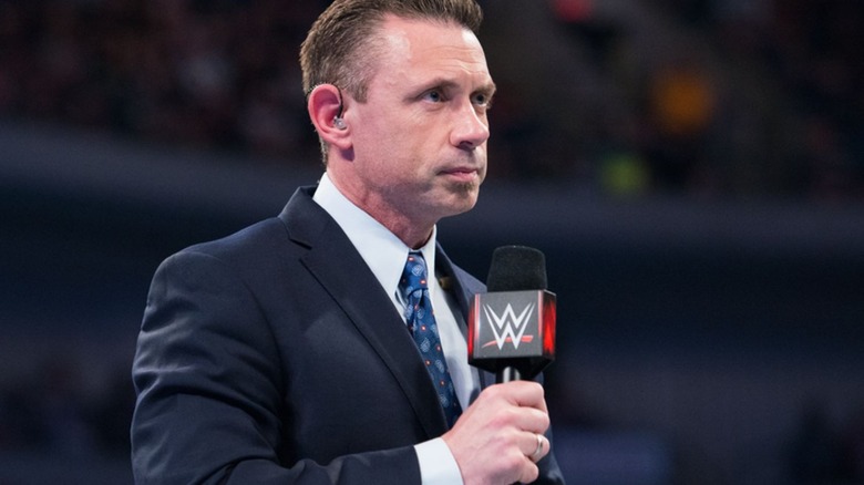 Michael Cole stands in the ring with a microphone