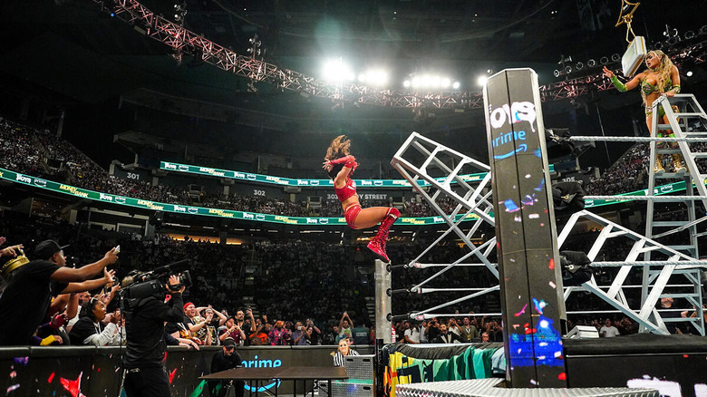 Tiffany Stratton waves goodbye to Chelsea Green as she falls from a ladder through some tables