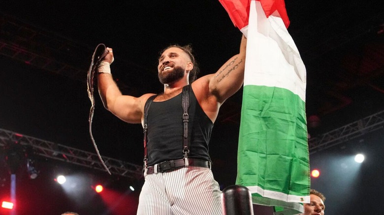 NXT North American Champion Tony D'Angelo stands holding the belt and the Italian flag on the ropes after his victory.