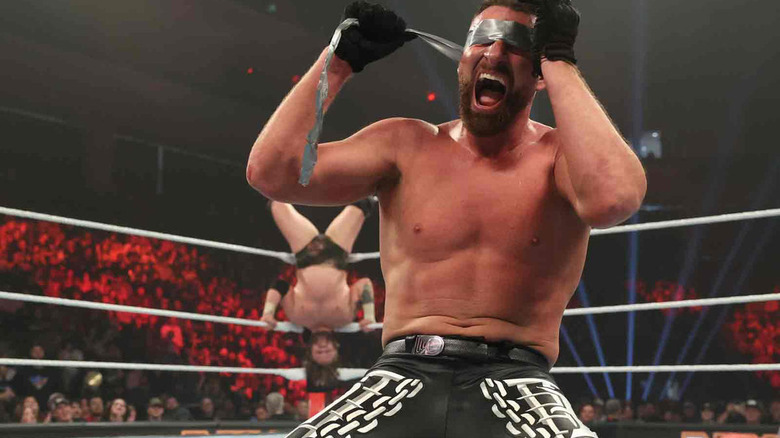 Dijak rips duct tape off his eyes while Joe Gacy poses upside-down behind him