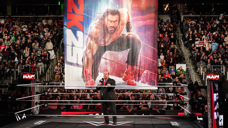 Paul Heyman stands in front of a poster of Roman Reigns on the cover of WWE 2K25 on "WWE Raw"