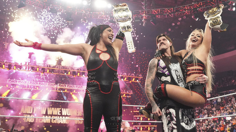 Raquel Rodriguez and Liv Morgan (in the arms of Dominik Mysterio) celebrate with their new women's tag titles as pyro goes off behind them on "WWE Raw"