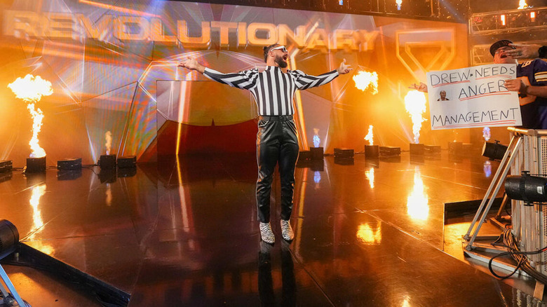 Seth Rollins in referee gear posing amidst pyro