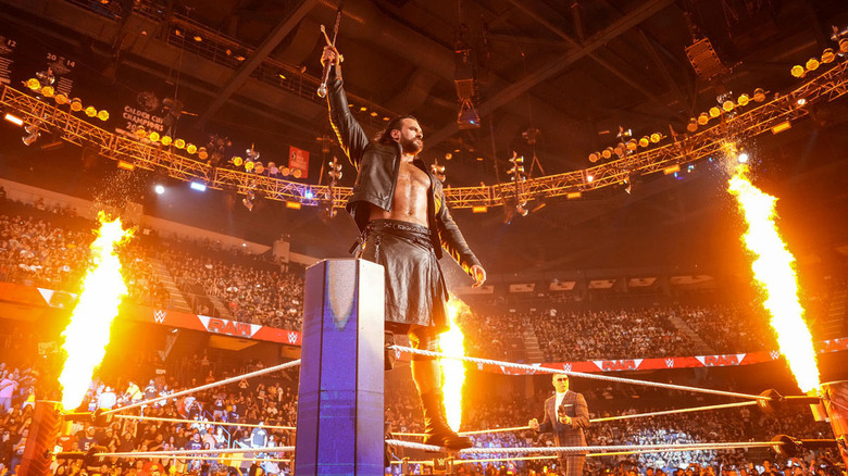 Drew McIntyre raises his sword while fire shoots up around him