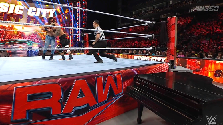 The two men locking up in the ring as the camera focuses on a piano