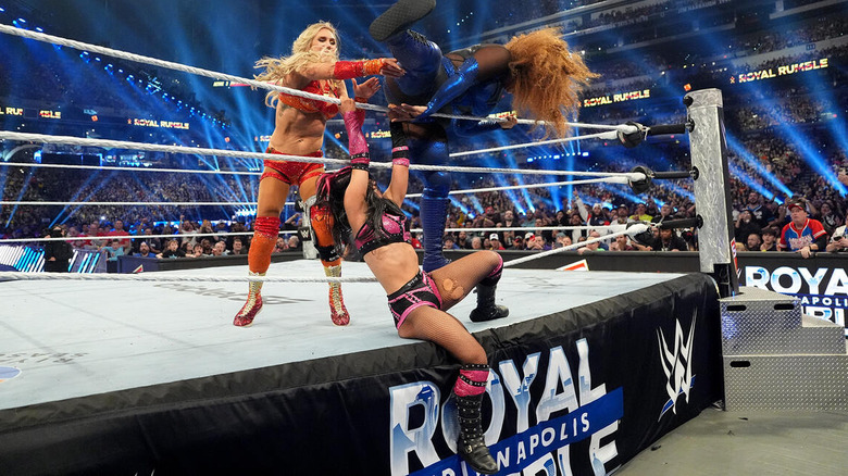 Charlotte Flair throws Nia Jax over the top rope while Roxanne Perez holds onto it at WWE Royal Rumble.