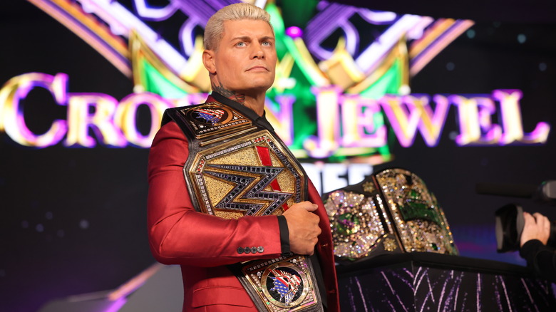 Cody Rhodes with WWE title belt over his shoulder while standing in front of the men's Crown Jewel Championship