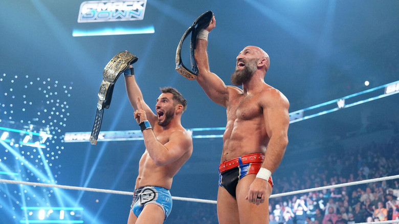 Johnny Gargano and Tommaso Ciampa hold up their tag title belts, grinning, on "WWE SmackDown.