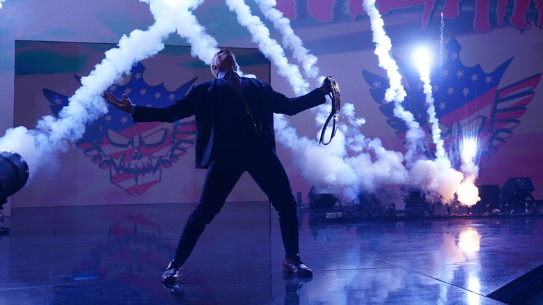 Cody Rhodes poses with his title while pyro goes off during his entrane