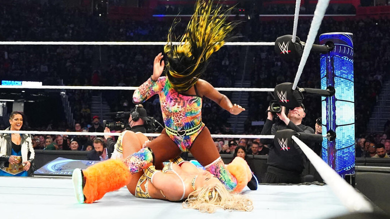 Naomi drops a leg on Tiffany Stratton while Bayley looks on