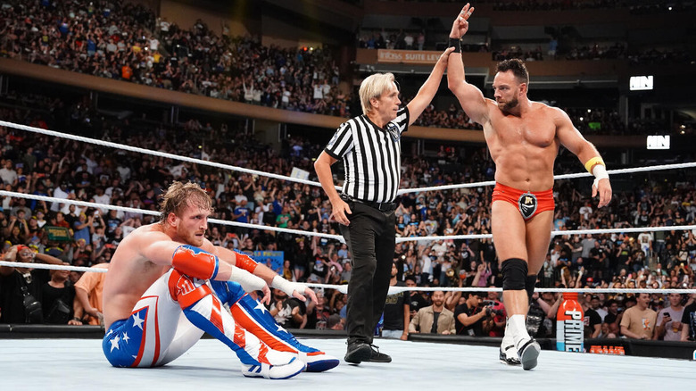 Referee raises LA Knight's hand while Logan Paul sits in the ring