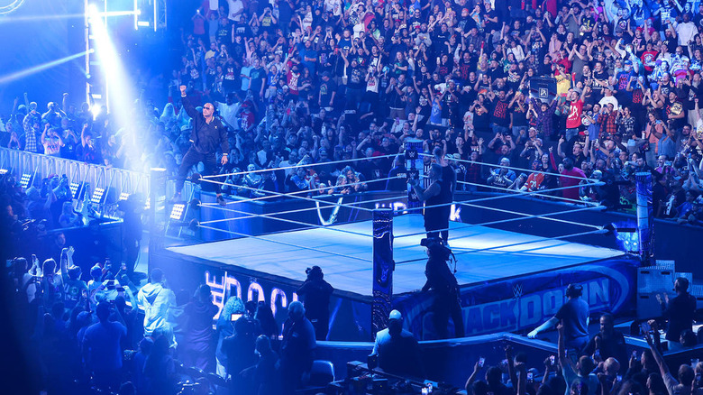 The Rock stands on a turnbuckle in the ring surrounded by fans