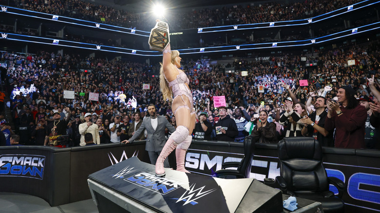 Tiffany Stratton holds up her title belt while standing on "WWE SmackDown" announce table