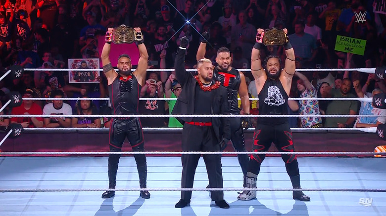 The Bloodline in the ring holding up their title belts and the One symbol