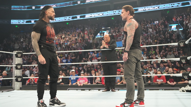 Roman Reigns and CM Punk stare each other down, as Paul Heyman looks on