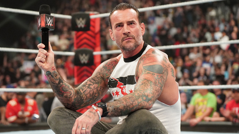 CM Punk, with a microphone in hand, sits in the middle of the ring about to give a speech to the 