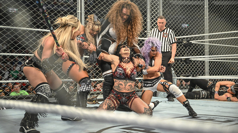 Nia Jax, Tiffany Stratton and Candice LeRae hold Rhea Ripley for Liv Morgan to hit with a baseball bat