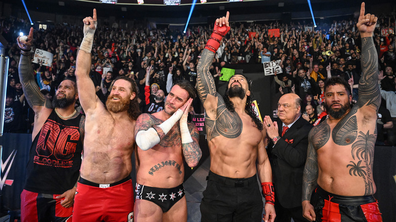 The OG Bloodline raises their ones in the air as CM Punk poses beside them