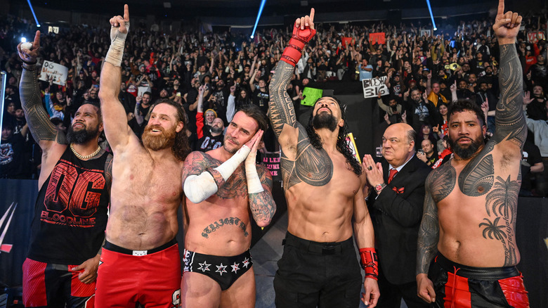 The OG Bloodline raises their ones in the air as CM Punk poses beside them at WWE Survivor Series