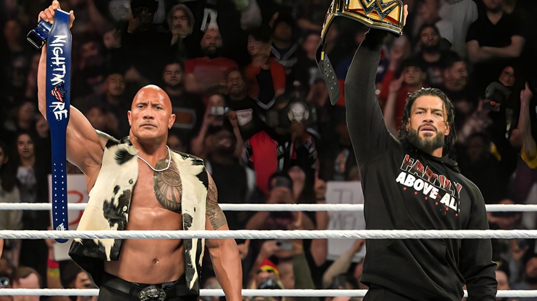 The Rock and Roman Reigns holding up belts