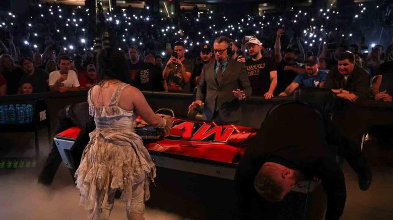 Abby the Witch hands Michael Cole a package at the commentary desk during an episode of "WWE Raw."