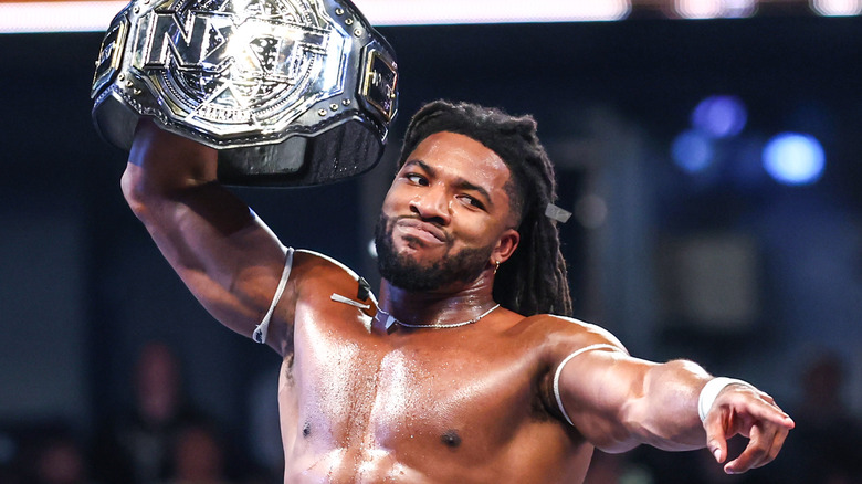 Trick Williams holds up the new "NXT" Championship as he points to the crowd.